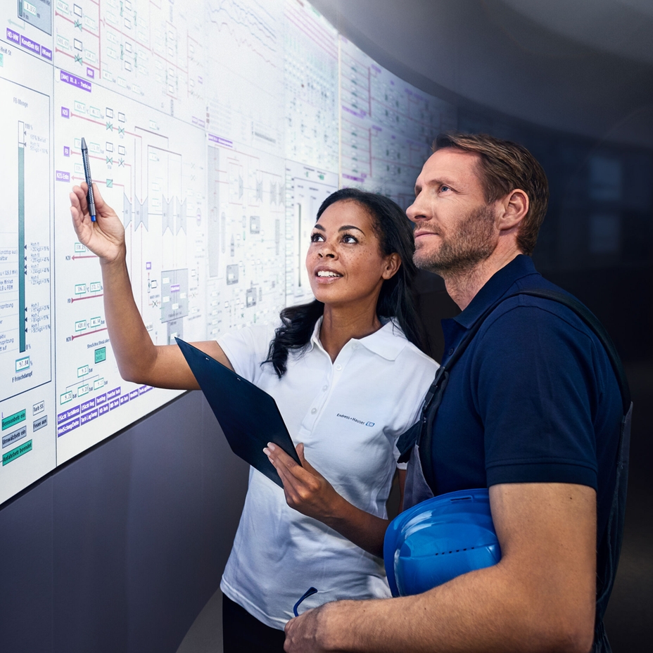 Two engineers look a a large display in an industrial control room.